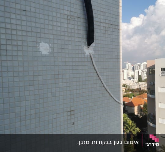 צינור שחור מחובר לקיר אריחים חיצוני